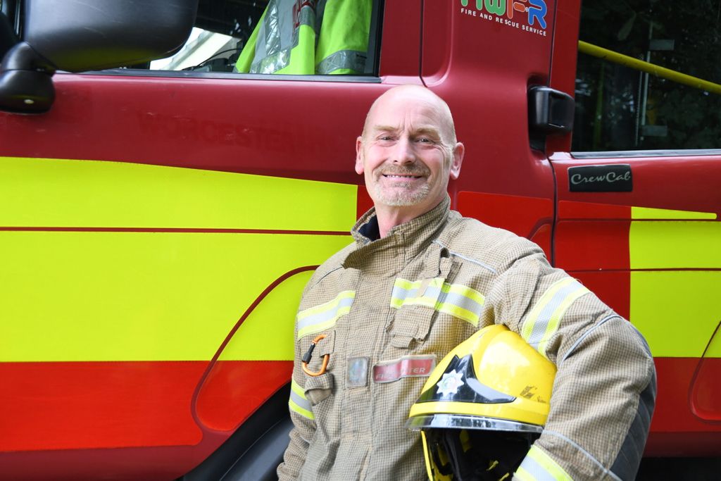 Firefighter holding helmet under arm in front of fire engine.