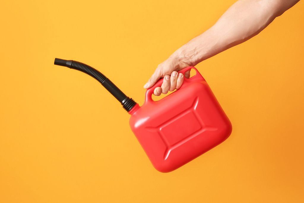 Male hand holding fuel canister with rubber nozzle on an orange background