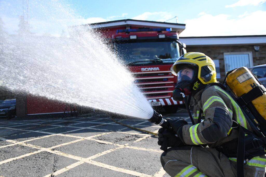 firefighter stooping down holding hose with water shooting out