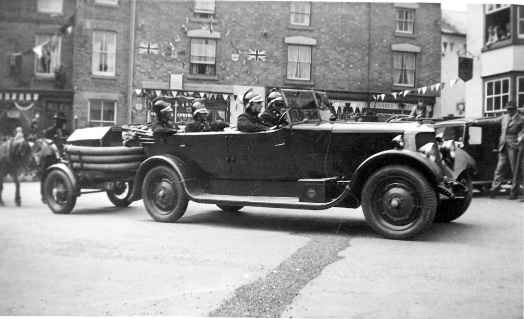 Fire vehicle with trailer in Bromyard town centre from 1930. Firefighter in car.