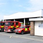 Three fire vehicles in front of fire station bays