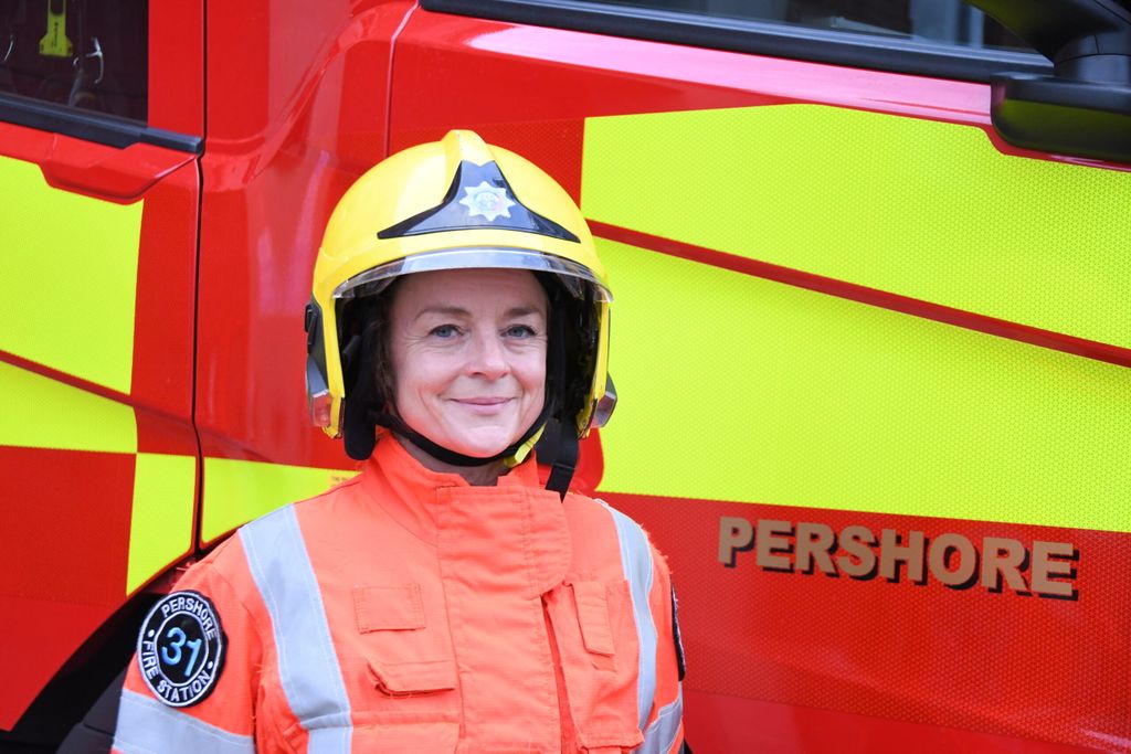 portrait of female firefighter with helmet on standing in front of fire engine