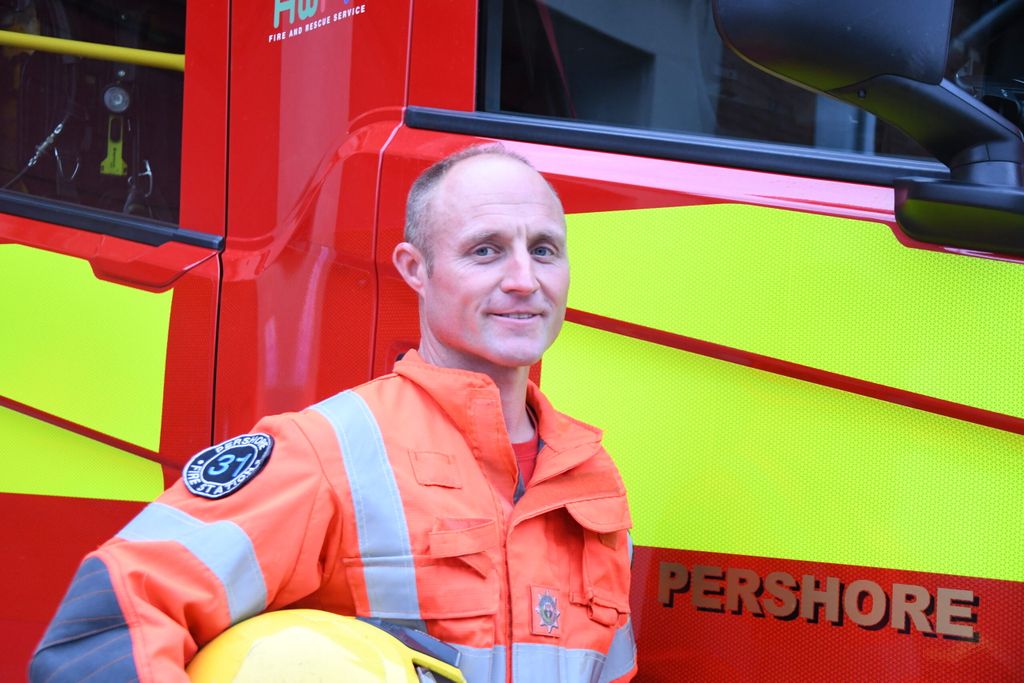 Firefighter holding helmet, standing in front of Pershore fire engine