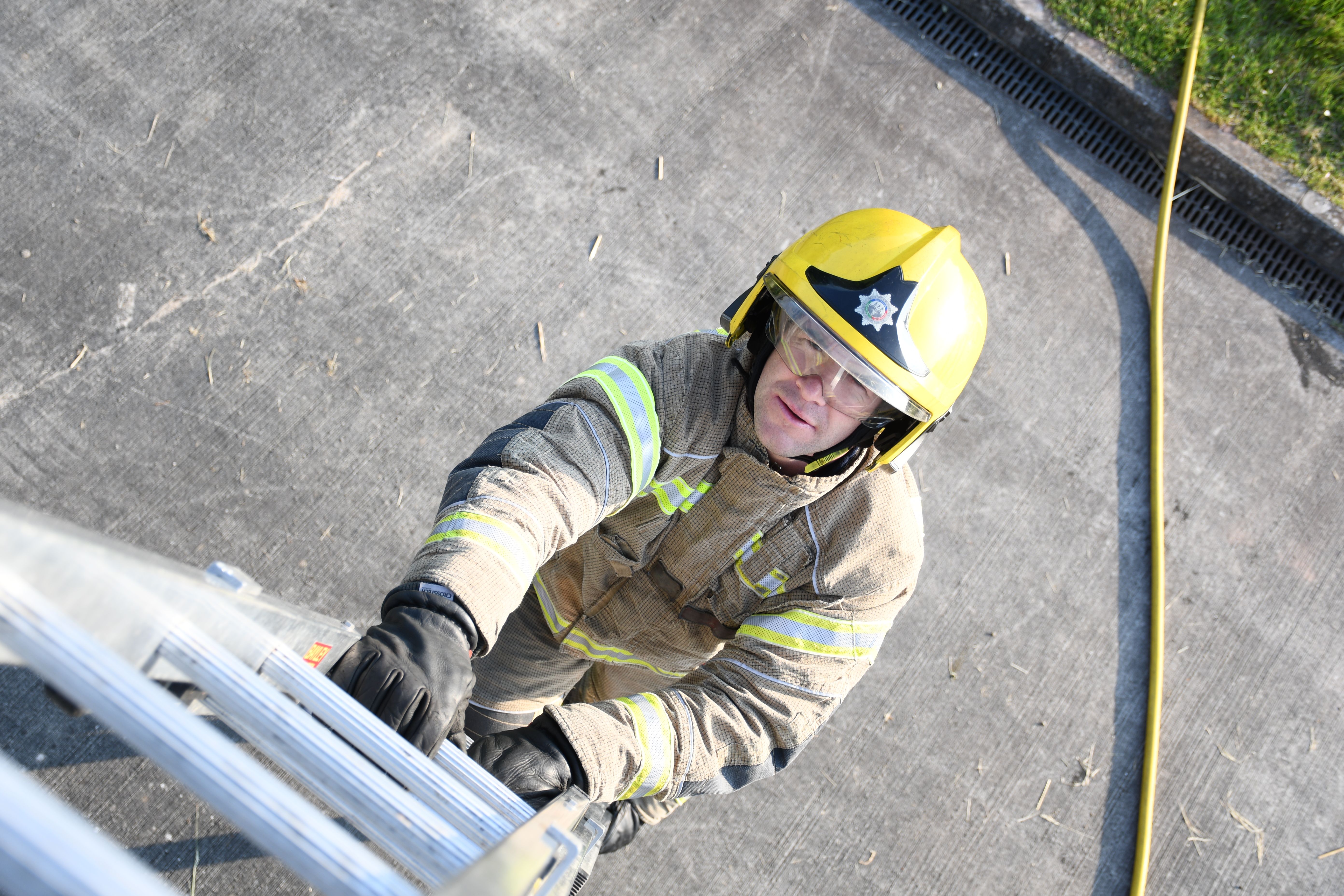 Firefighter in yellow helmet climbing up a ladder.