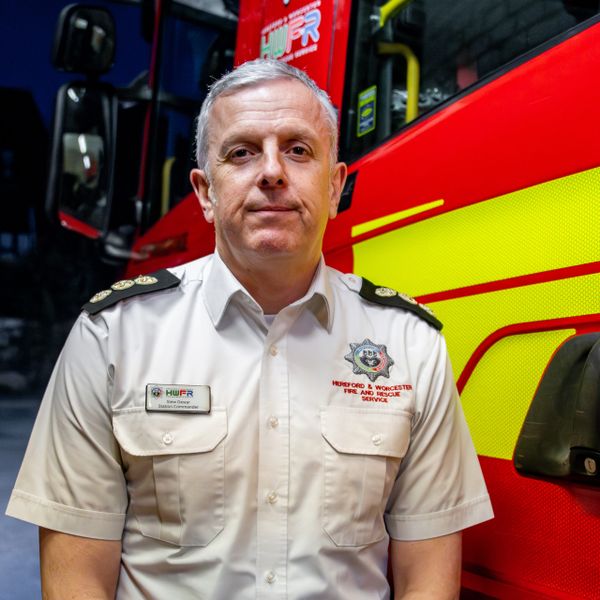 station commander standing in front of a fire engine in the bay of the fire station