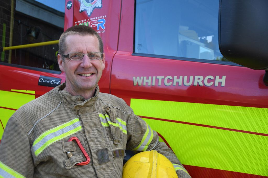 firefighter holding helmet standing in front of fire engine